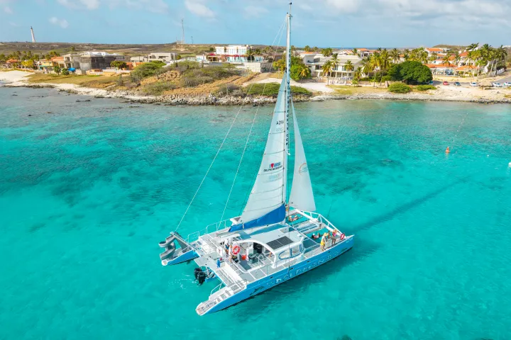 Catamaran on turquoise waters near a coastal town with sandy beaches.
