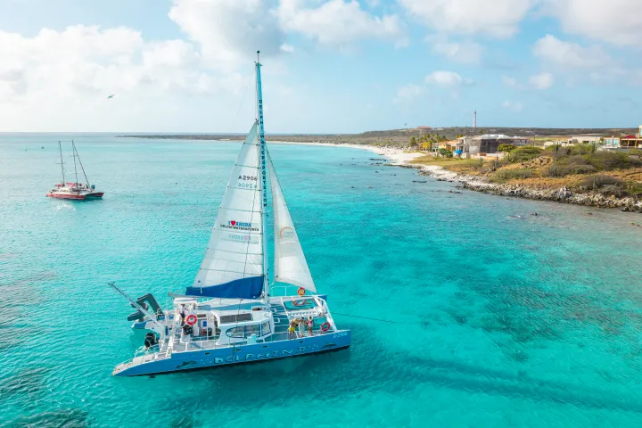 Sailboat on clear turquoise water near a coastline with a distant sailboat.