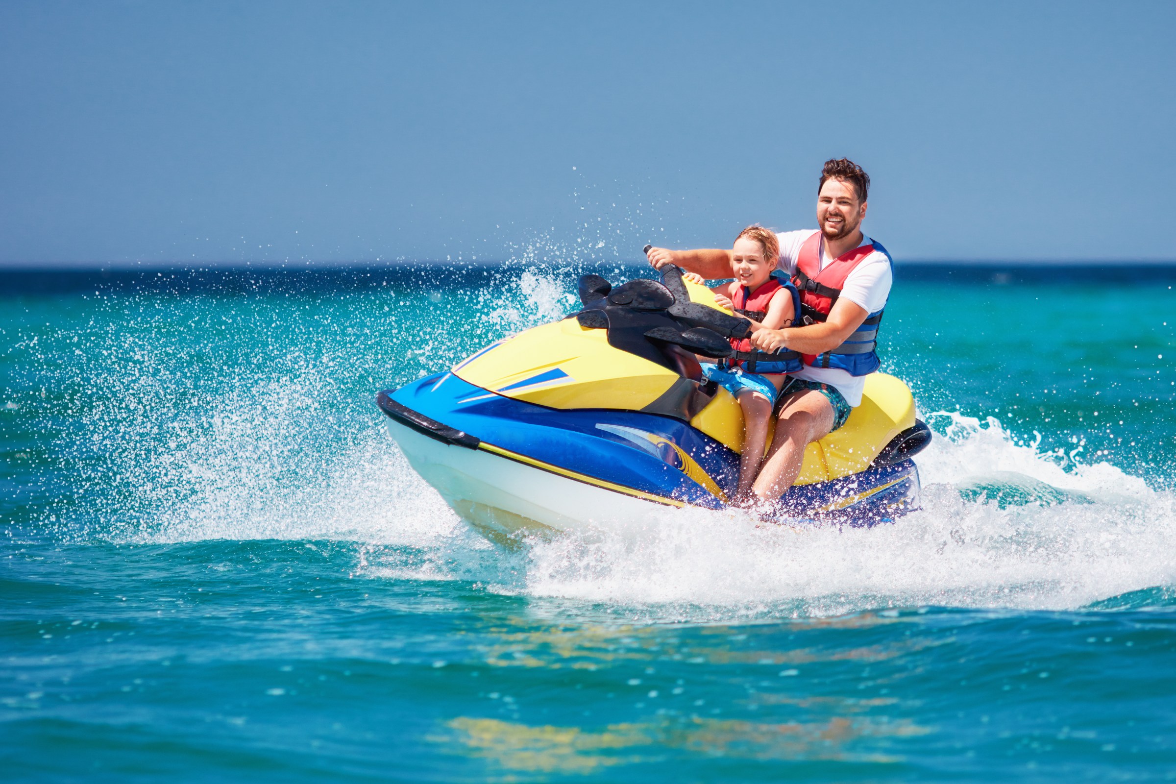 Happy father and son having fun on a jet ski during vacation in Aruba.