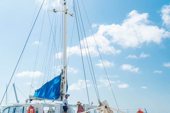 People boarding a blue catamaran on a sunny beach.