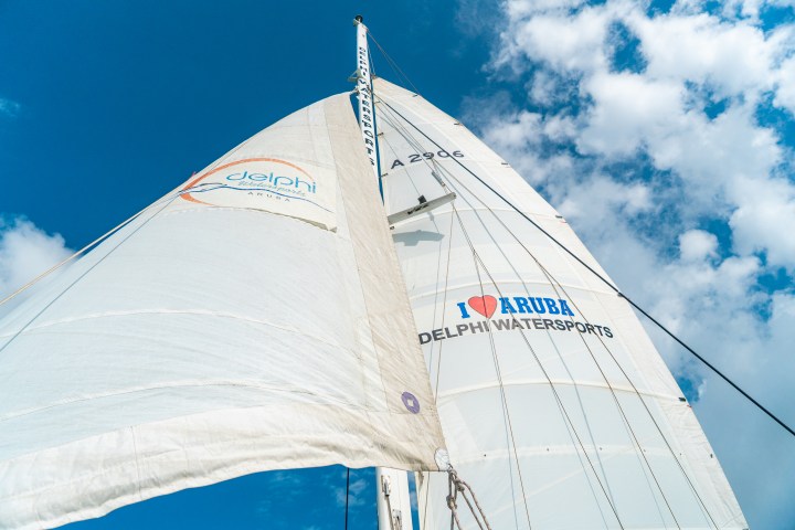 Sailboat sails with 'I Love Aruba Delphi Watersports' logo against a blue sky.