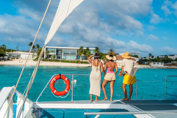 Three people on a boat near tropical shore with clear blue water.