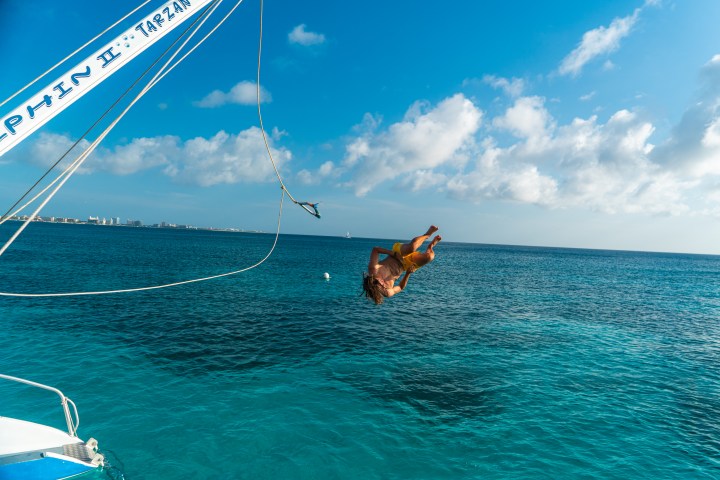 Person flips off a boat into the ocean under a clear blue sky.