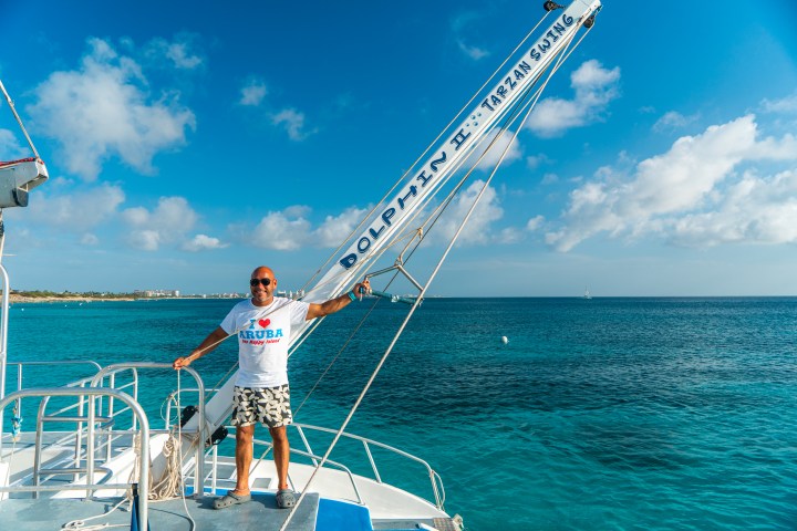 Man on boat deck near ocean, holding a pole with 'Dolphin H. Tarzan Swing' text.
