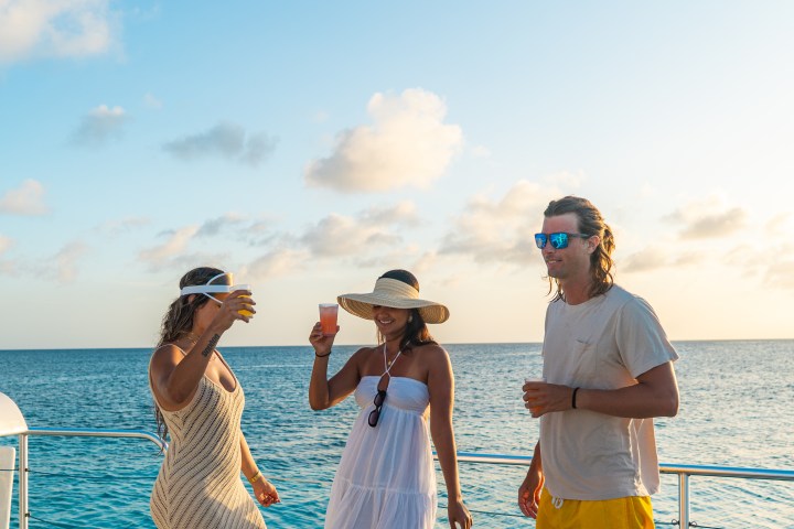 Three people enjoying drinks on a boat at sunset with ocean view.